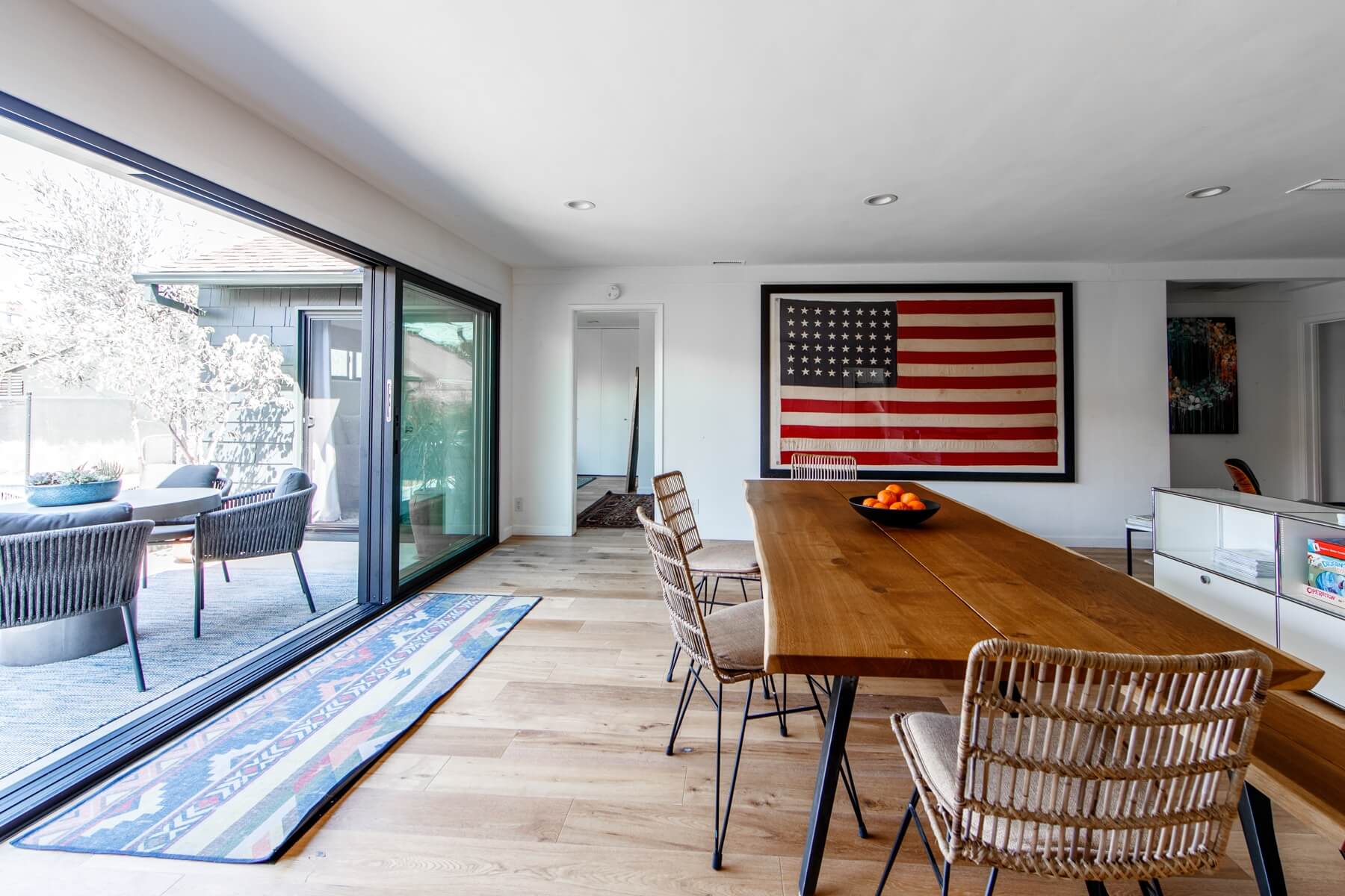 outdoor patio behind glass doors, inside wooden table with oranges in a bowl and American flag artwork