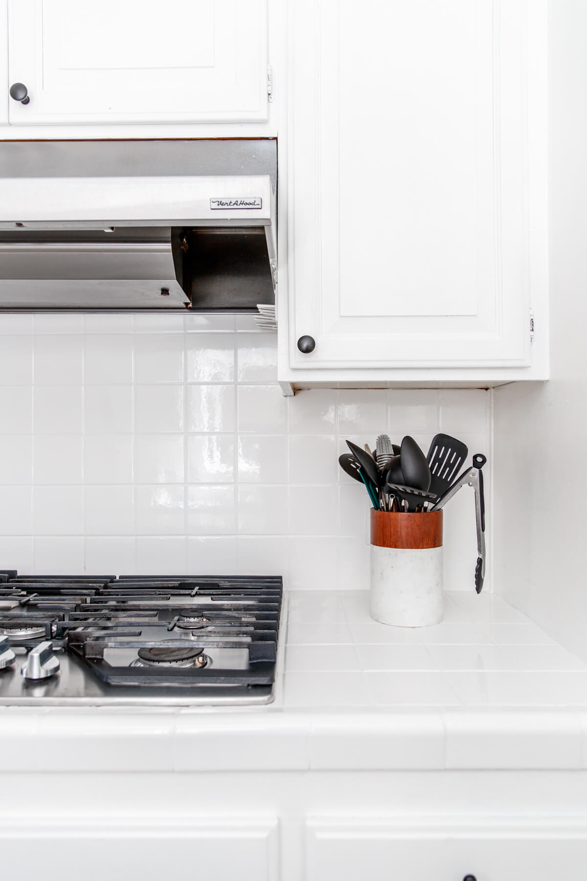 stovetop, hood, and utensils on white tile countertop