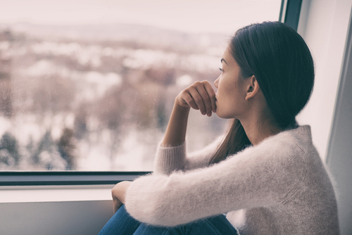 woman looking out a window being sad