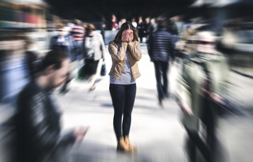 woman standing with her head in her hands while everyone around is blurry